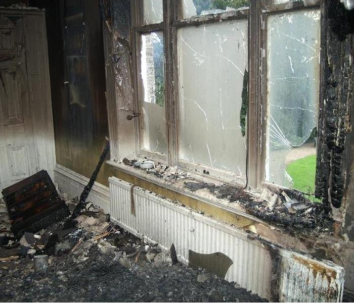 Badly damage wall with broken glass windows covered in soot and surrounded by debris
